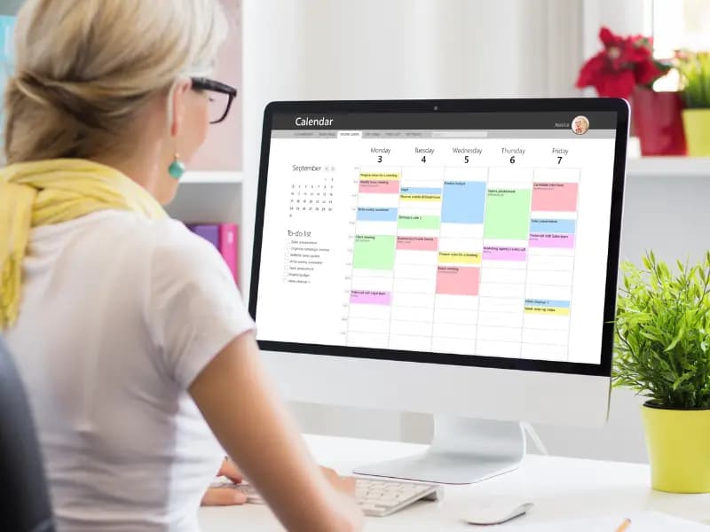 Appointment scheduling on a desktop screen while a woman organizes her weekly tasks in a well-lit office.